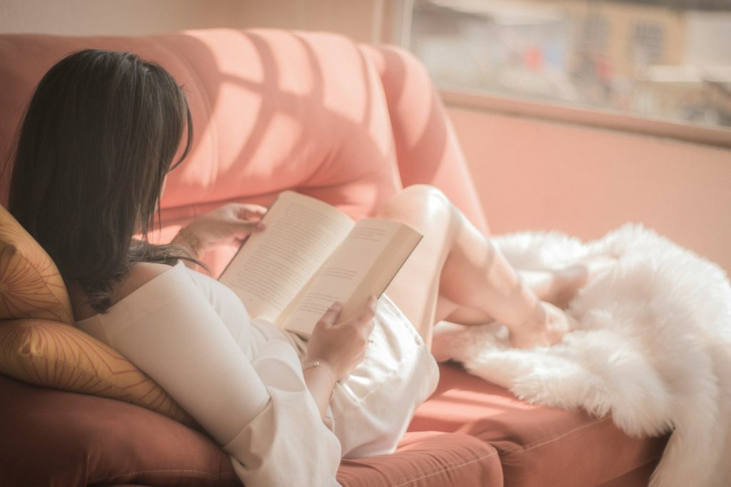 woman holding self help book sitting on pink fabric sofa