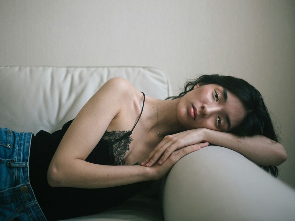 woman wearing black spaghetti-strap tank top and blue denim bottoms lying on sofa, can't sleep, reflecting signs of overthinking