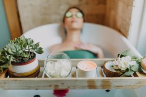 Woman relaxing in a bathtub with a candle and plants, enjoying a serene spa experience. Blog post about self care ideas for women.