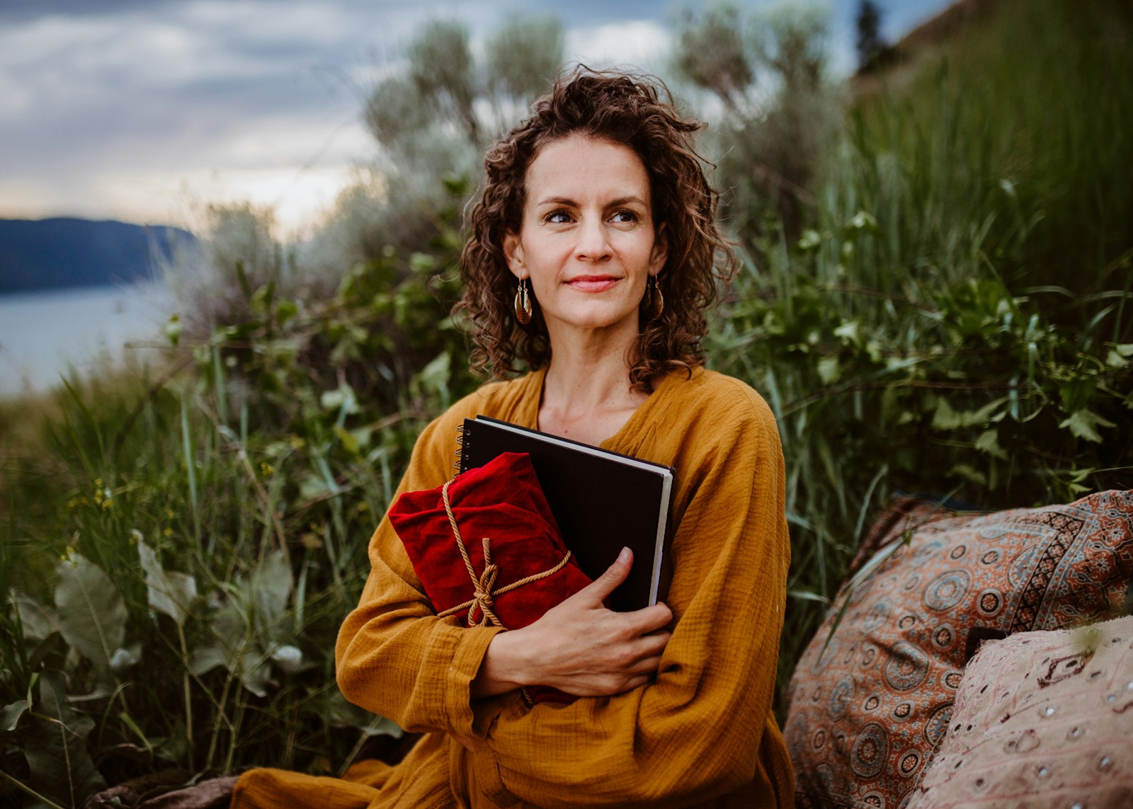 A woman sitting on a rock holding a book, for a post about self care gifts for women and self care gifts ideas