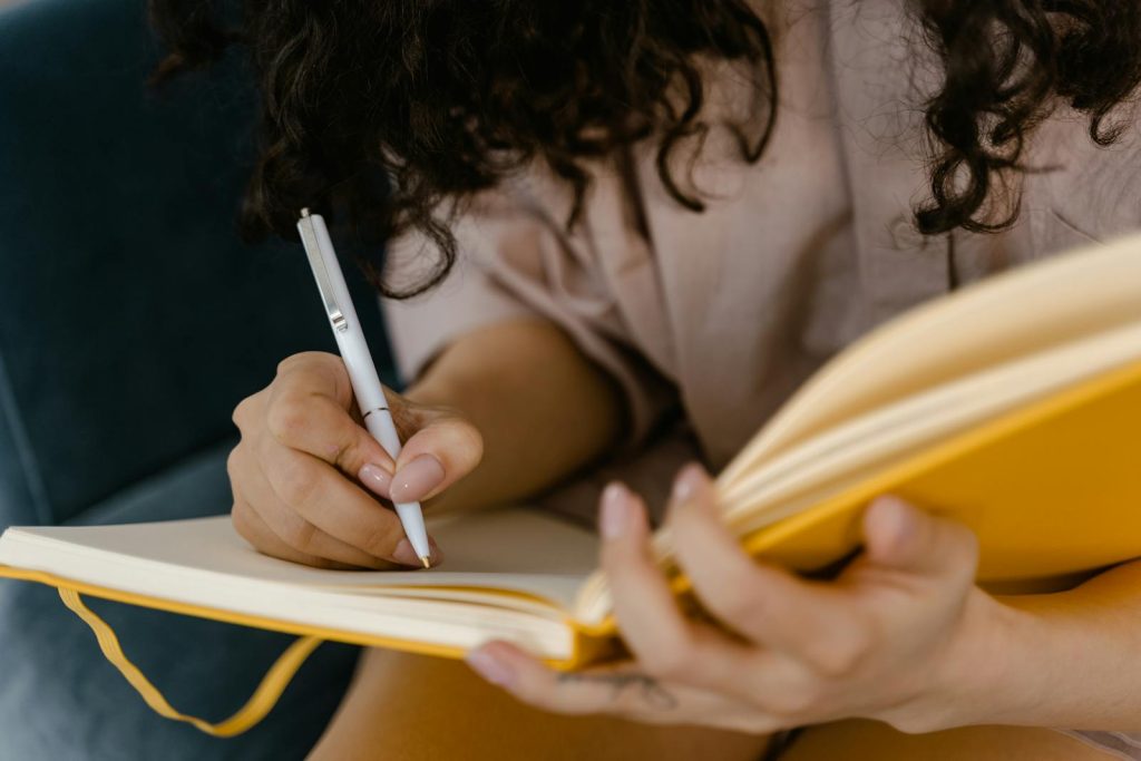 Person writing in a yellow notebook indoors, focusing on ideas, guided mindfulness journal with daily prompts and affirmations to support calm and reflection 