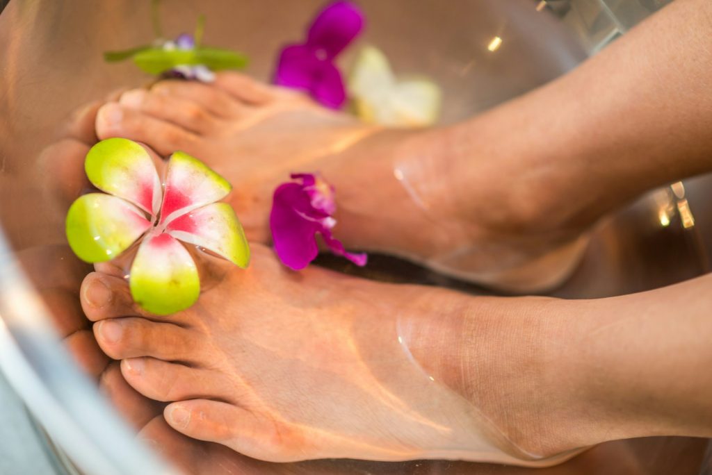 person's feet with flowers, heated foot bath with water bubbles and massage rollers for relaxation and stress relief 