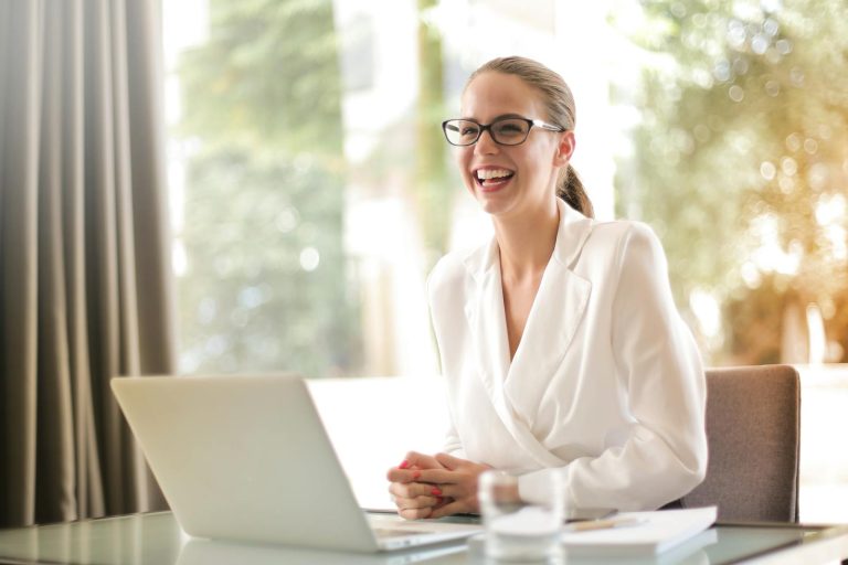 Cheerful businesswoman in glasses working on a laptop, in a bright and modern office setting. represents corporate wellness programs or employee wellness programs