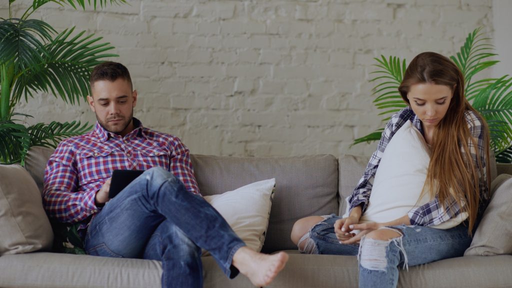 Couple sitting on sofa looking at phones, unhealthy relationship, insecure relationship