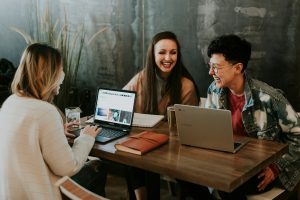 three people sitting in front of table laughing together, happy emotionally regulated employees at work