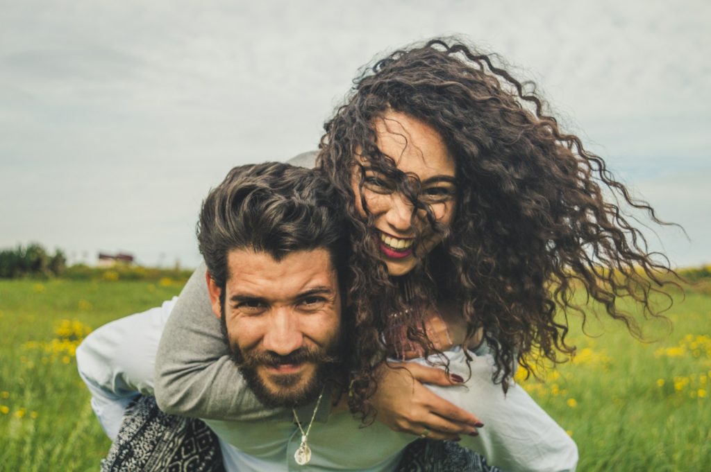woman riding on man's back on green field, happy couple, happy relationship