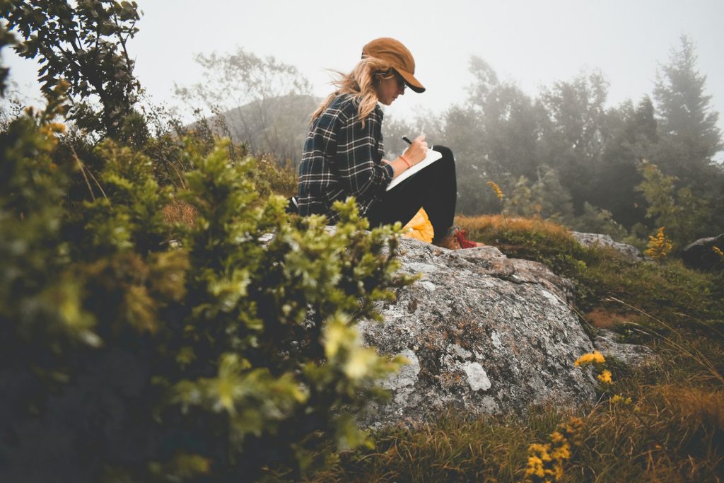 a woman sitting on top of a rock writing, journaling for self-care