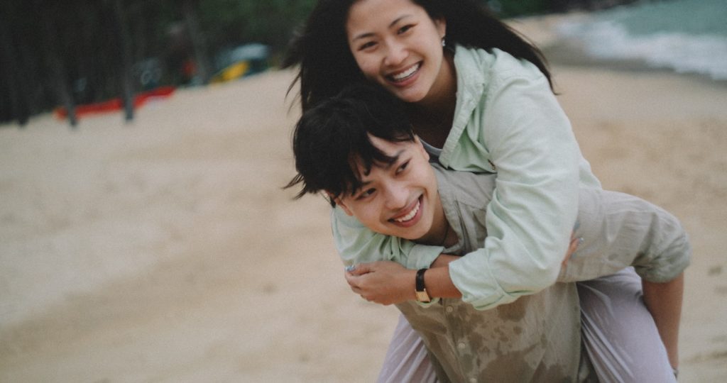 Couple enjoys a piggyback ride on a sandy beach. blog post about healthy relationships