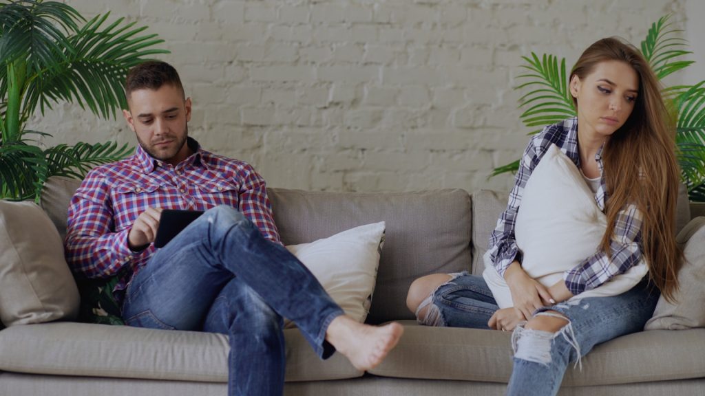 Couple sitting apart on a sofa, looking away unhappy couple in relationship