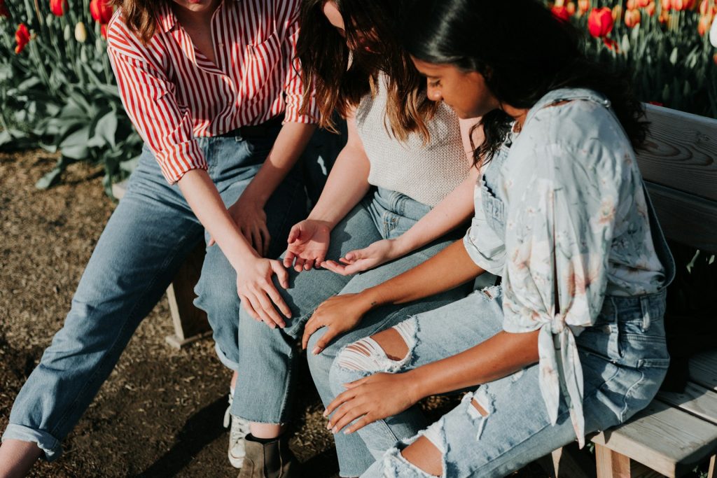 three women wearing blue denim jeans sitting on gray wooden bench, support group