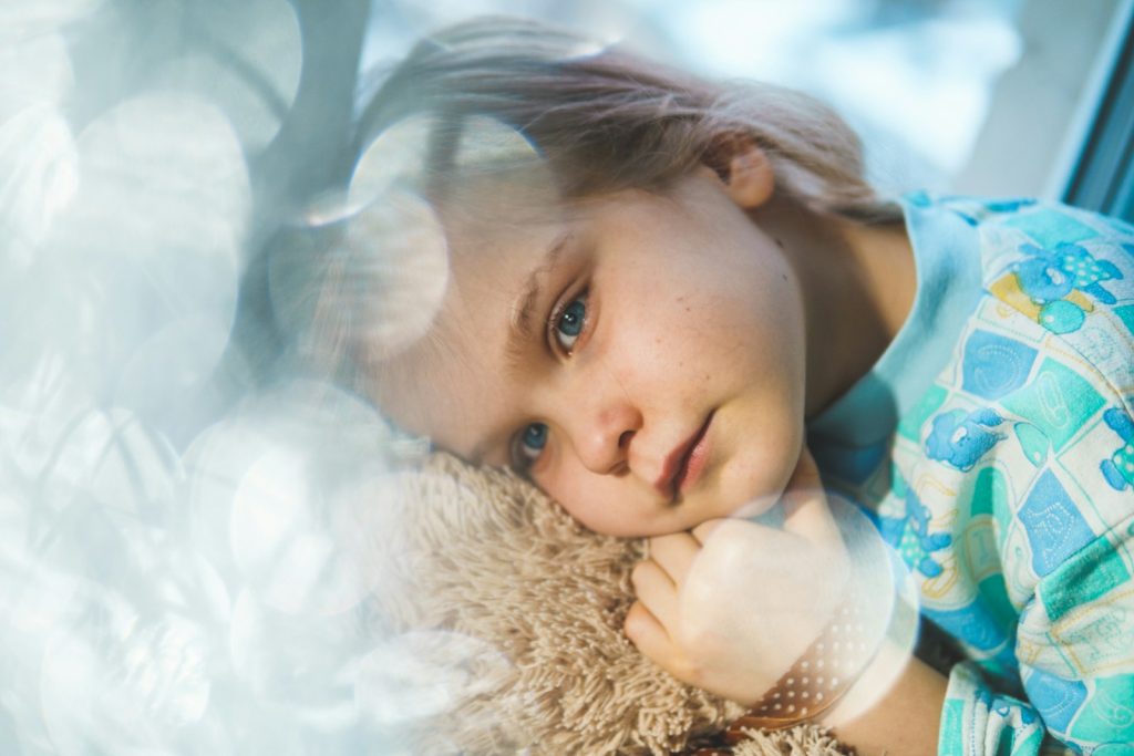 girl in white and blue floral dress lying on white fur textile she looks sad, blog post talking about BPD and childhood trauma 