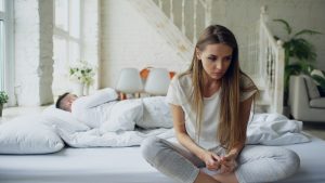 Woman sitting on bed, man sleeping behind her. unhappy couple, blog post about dating someone with bpd