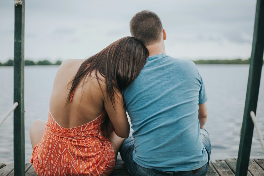 man and woman sitting on dock viewing calm sea, feel safe in relationships