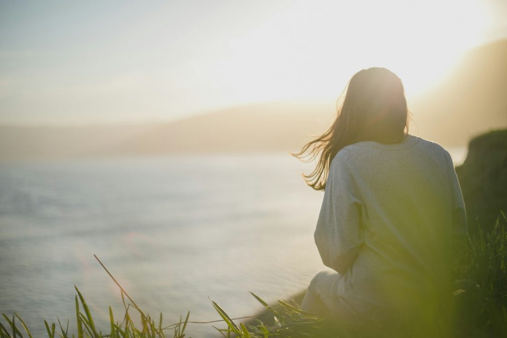 woman wearing gray long-sleeved shirt facing the sea practing acceptance