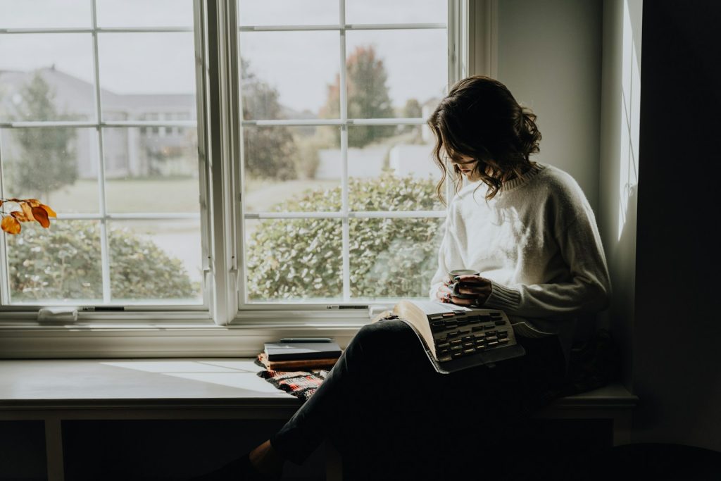 woman sitting by window - Blair Nicole | Mental Health, Relationships, Travel A woman sitting on a window sill reading a book