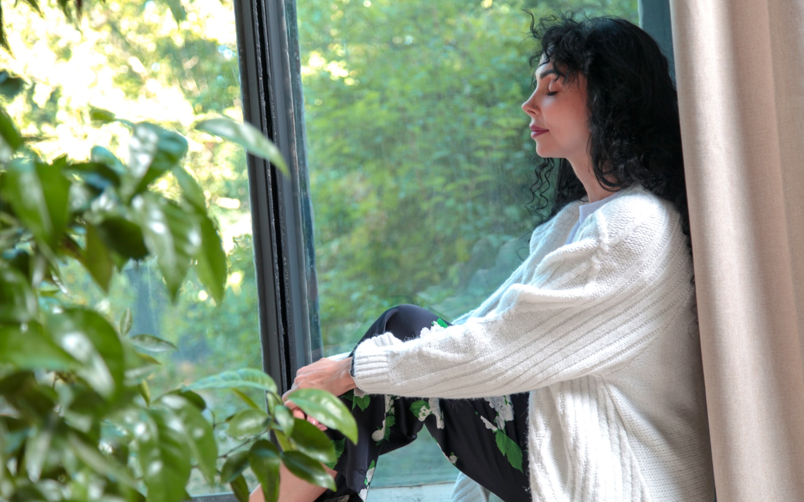 a woman sitting on a window sill looking out the window practicing radical acceptance