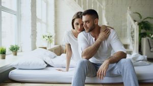 Couple sitting on a bed in a bright room struggling with addiction in relationships